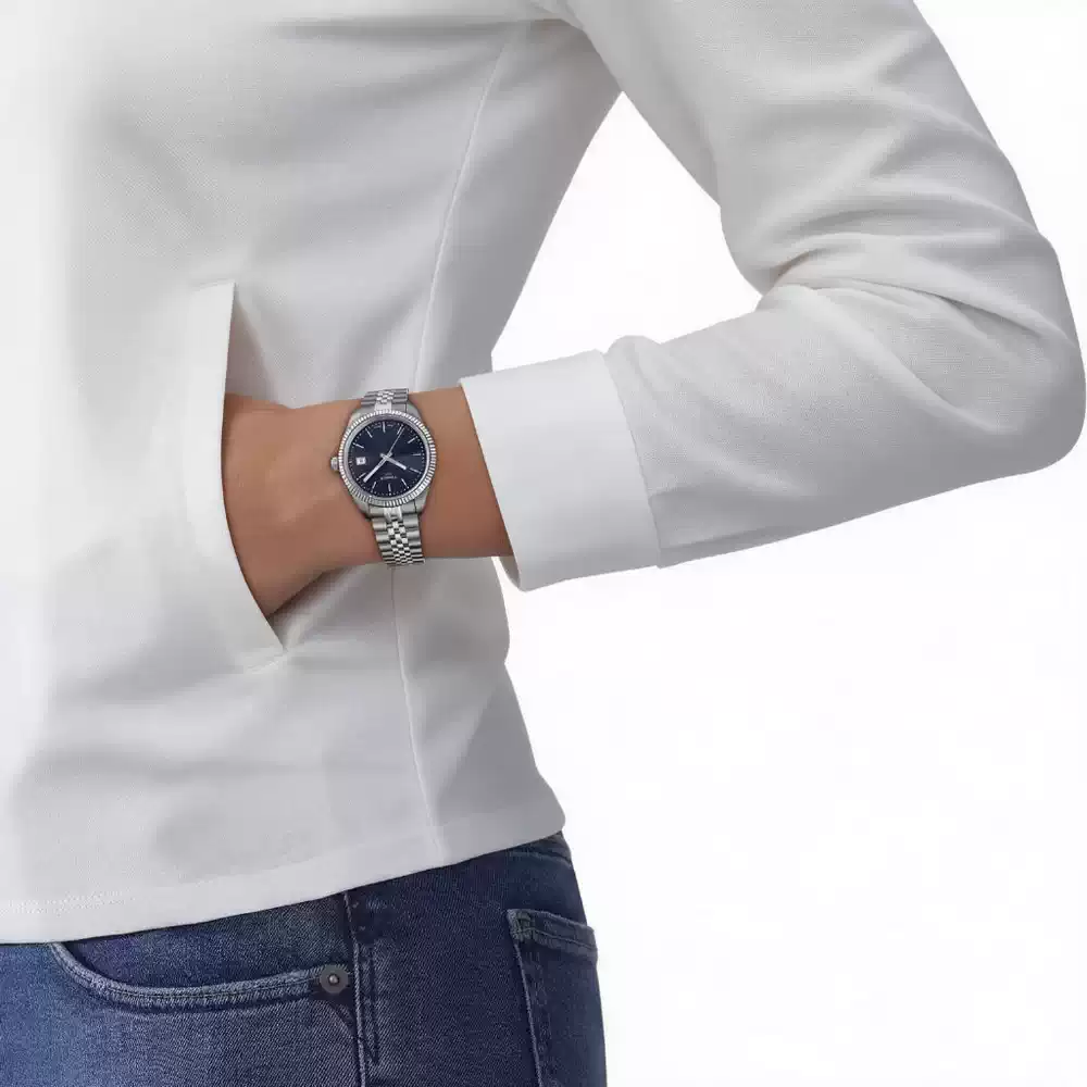 Mujer luciendo un Tissot Ballade de esfera azul con camisa blanca y jean