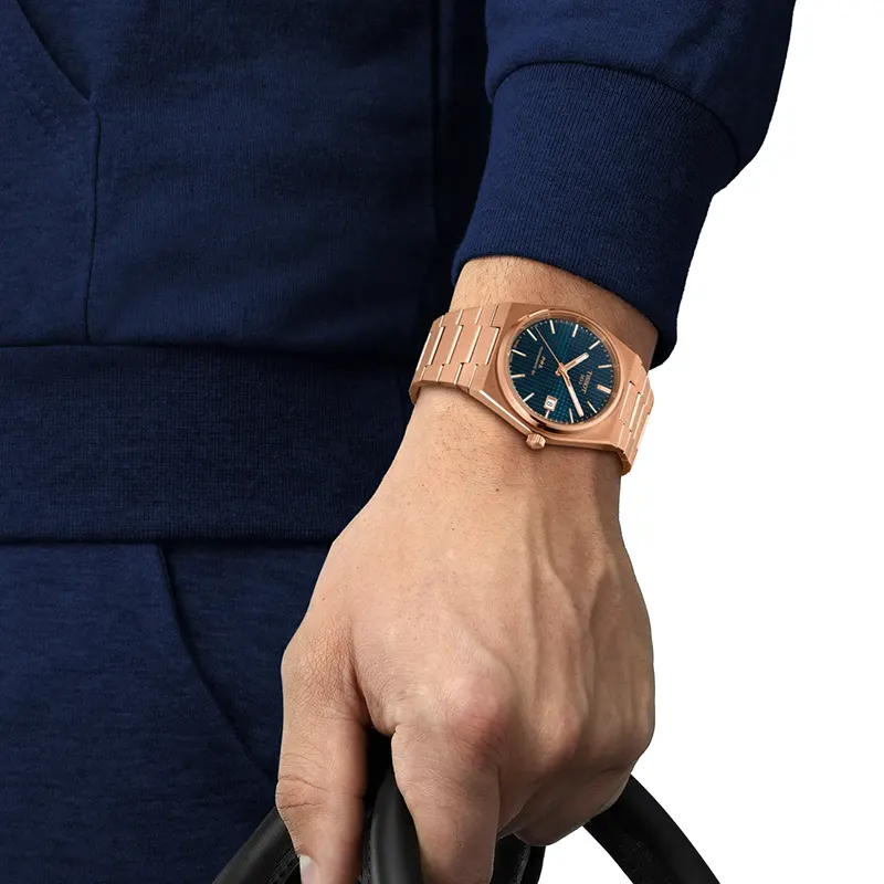 Tissot PRX de 40 mm con esfera azul y malla color oro rosa puesto con indumentaria azul