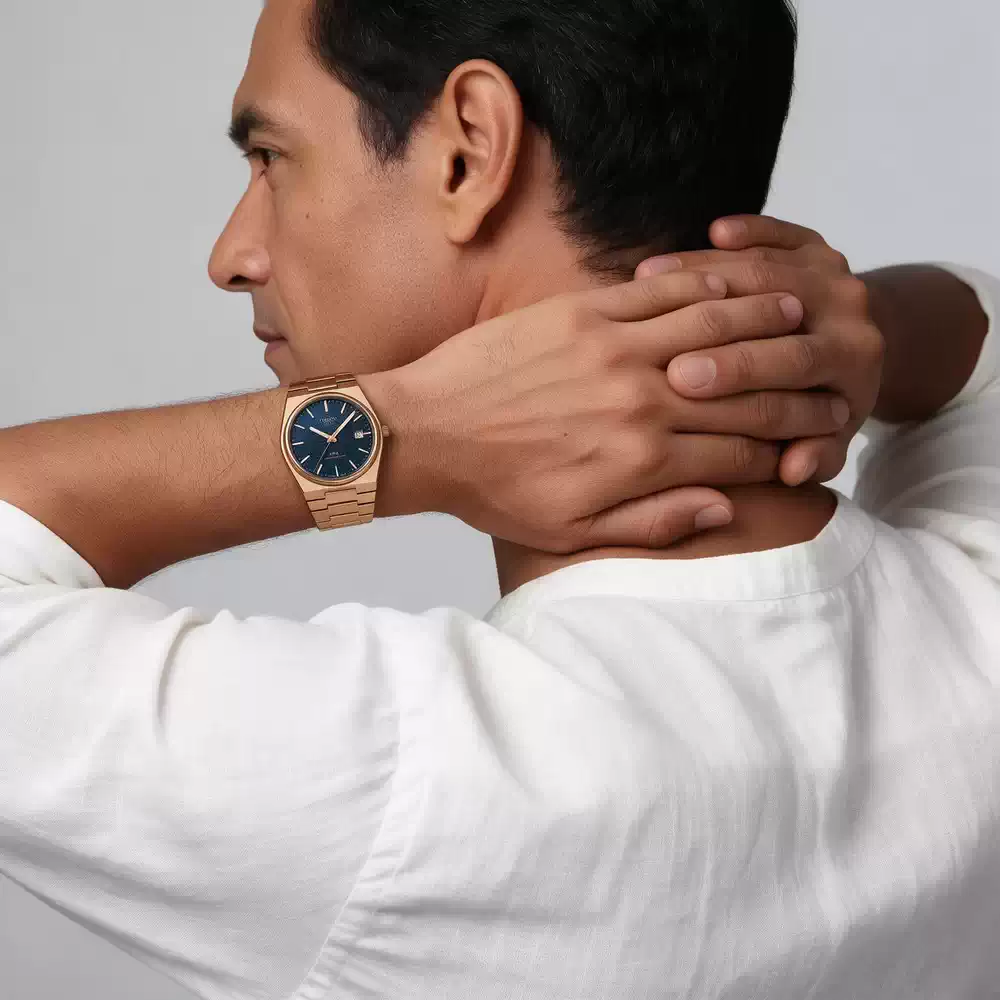 Hombre con camisa blanca llevando el Tissot PRX color oro rosa y esfera azul en la muñeca